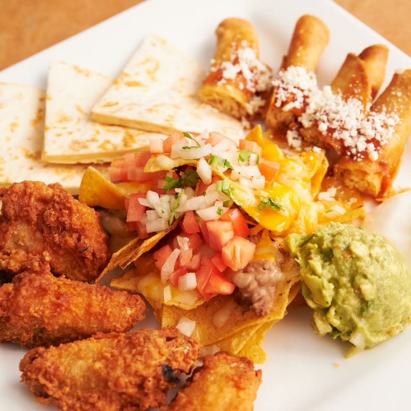 Acapulcos Mexican appetizer platter with quesadillas, taquitos, nachos, fried chicken, guacamole, and sour cream.
