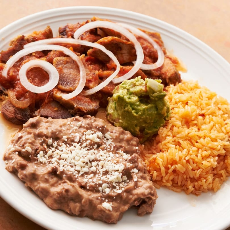 Acapulcos Mexican dish with saucy meat, onion rings, guacamole, refried beans, and rice.