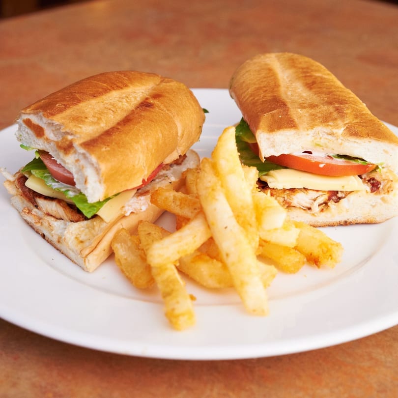 Two Mexican torta sandwiches with chicken, cheese, lettuce, and tomato, served with fries.