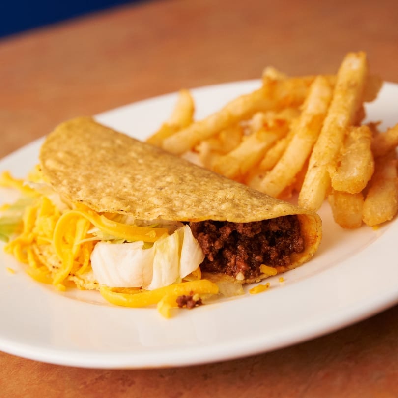 A crispy beef taco with lettuce and cheese, served with a side of golden french fries.